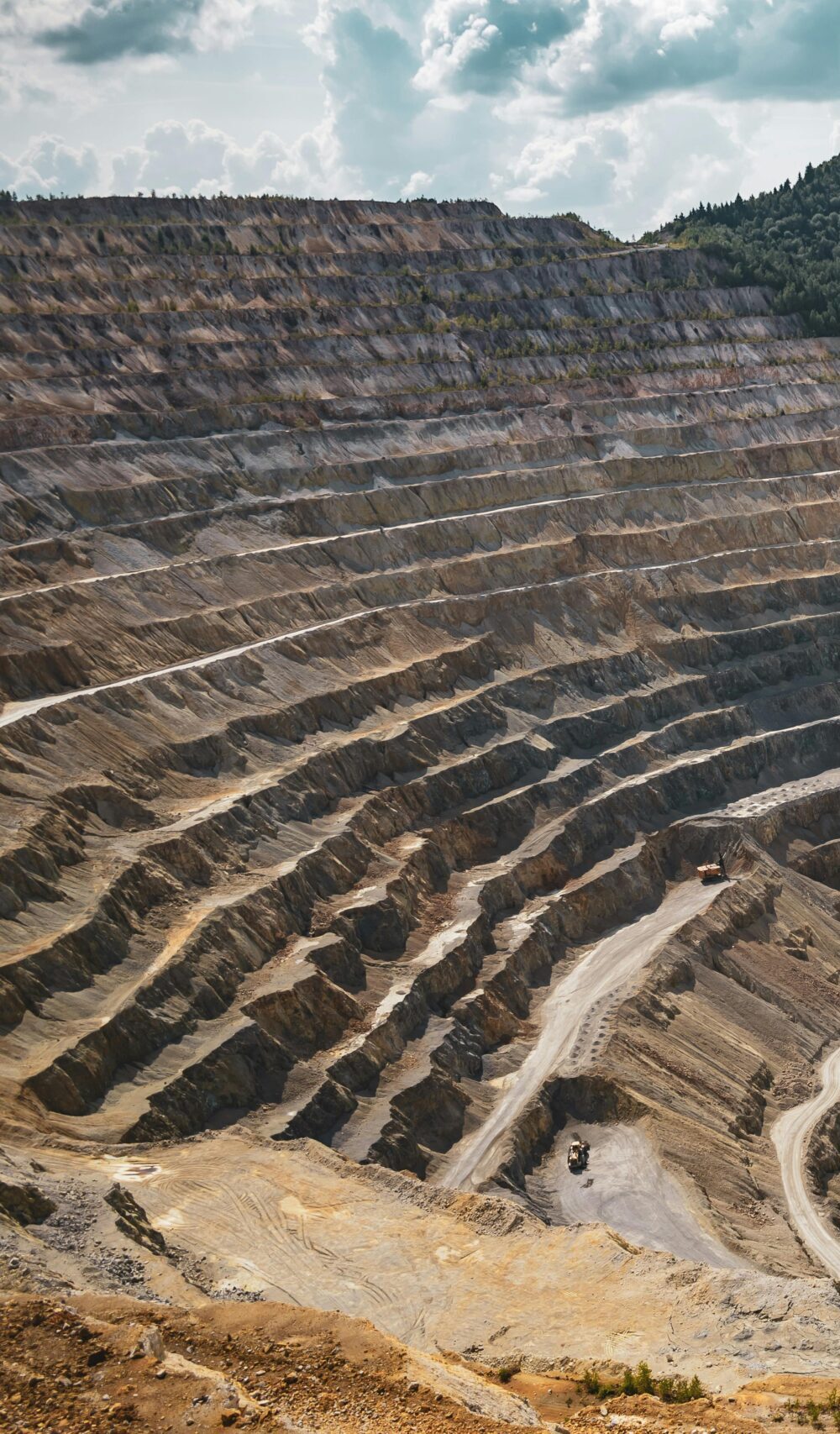 Aerial view of a large open-pit mine with terraced excavation during summer.